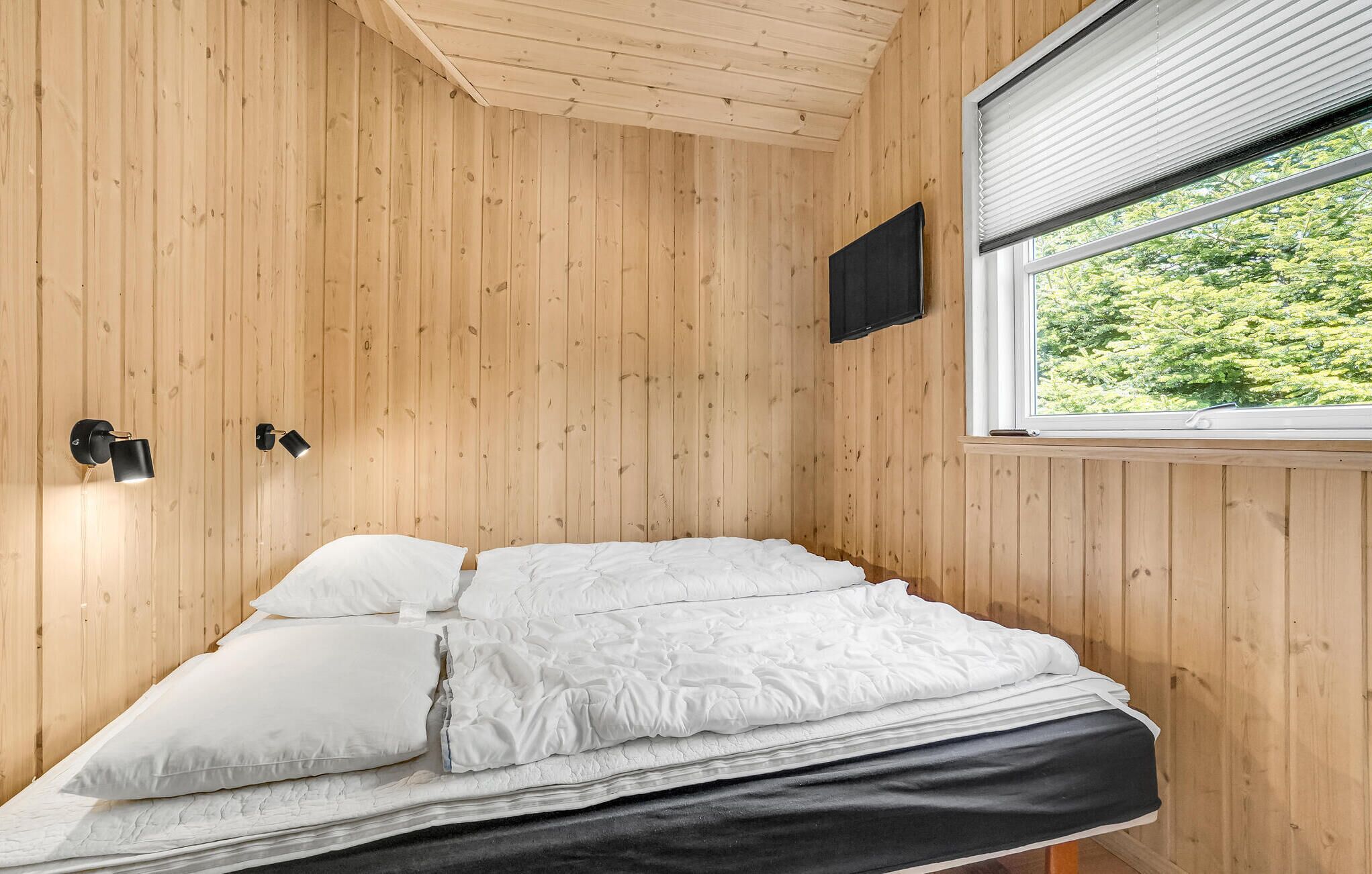 A single bed with white bedding in a room with wooden walls and a window with blinds.