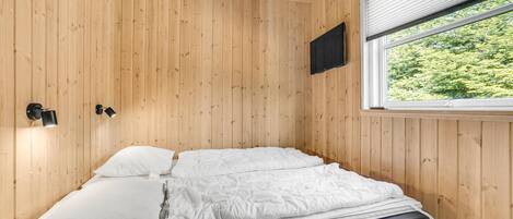 A single bed with white bedding in a room with wooden walls and a window with blinds.