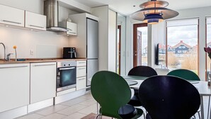 Une cuisine moderne avec des meubles blancs, des appareils en acier inoxydable et un coin repas doté de chaises vertes et noires.