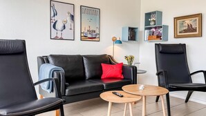 Un salon moderne avec un canapé en cuir noir, deux fauteuils noirs, une petite table en bois et une télécommande posée dessus.