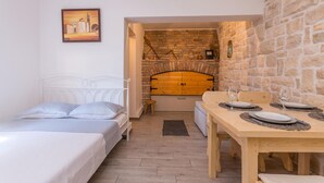 Una habitación acogedora con una cama, un taburete pequeño, una mesa de comedor dispuesta con platos y vasos, y una pared de piedra con chimenea.