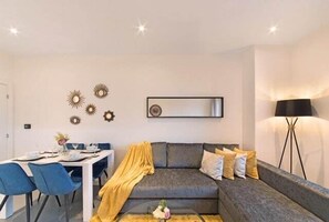 A modern living room with a grey sofa, a dining table with chairs, and a coffee table.