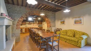 A dining area with a long wooden table and chairs, a stone archway, a kitchen in the background, and a patterned sofa. - Gorgeous home in Arezzo (Arezzo)