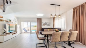 A modern living room with a dining area, a TV, and a view of the outdoors. - Cozy home in Linardici (Linardici)