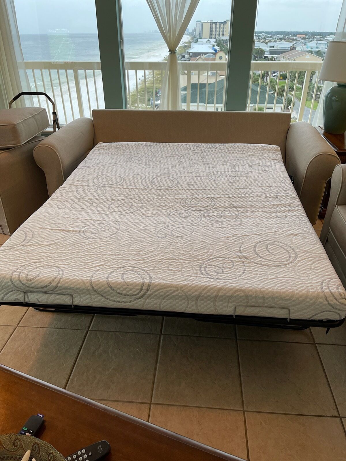 Un sofá cama convertible con un colchón estampado en una habitación con vista al océano y a edificios.