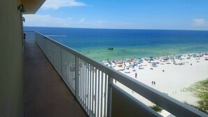 A balcony with a view of a beach with people and umbrellas.