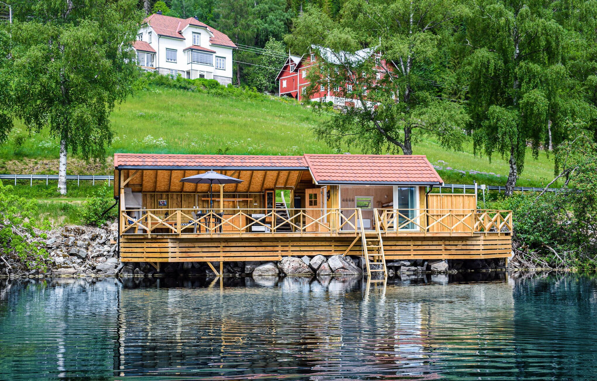 Une maison flottante en bois dotée d’une terrasse, d’un espace salon extérieur couvert et offrant une vue sur le lac.