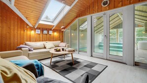 A cozy room with a wooden ceiling, a sofa, a coffee table, and a large sliding glass door leading to an outdoor area. - Beautiful home in Sydals with sauna (Sydals)