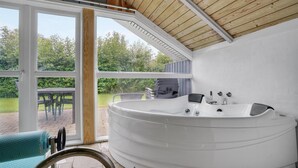 A modern bathroom with a large white bathtub, a shower, and a glass door leading to an outdoor patio with a table and chairs. - Beautiful home in Sydals with sauna (Sydals)