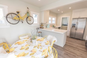 Une cuisine moderne dotée d’un îlot central, d’un réfrigérateur encastré et d’un coin repas avec une table ornée d’un motif citron.