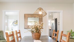 Un coin repas avec une grande table, des chaises en bois, un luminaire suspendu en fibres tressées et un vase rempli de fleurs.