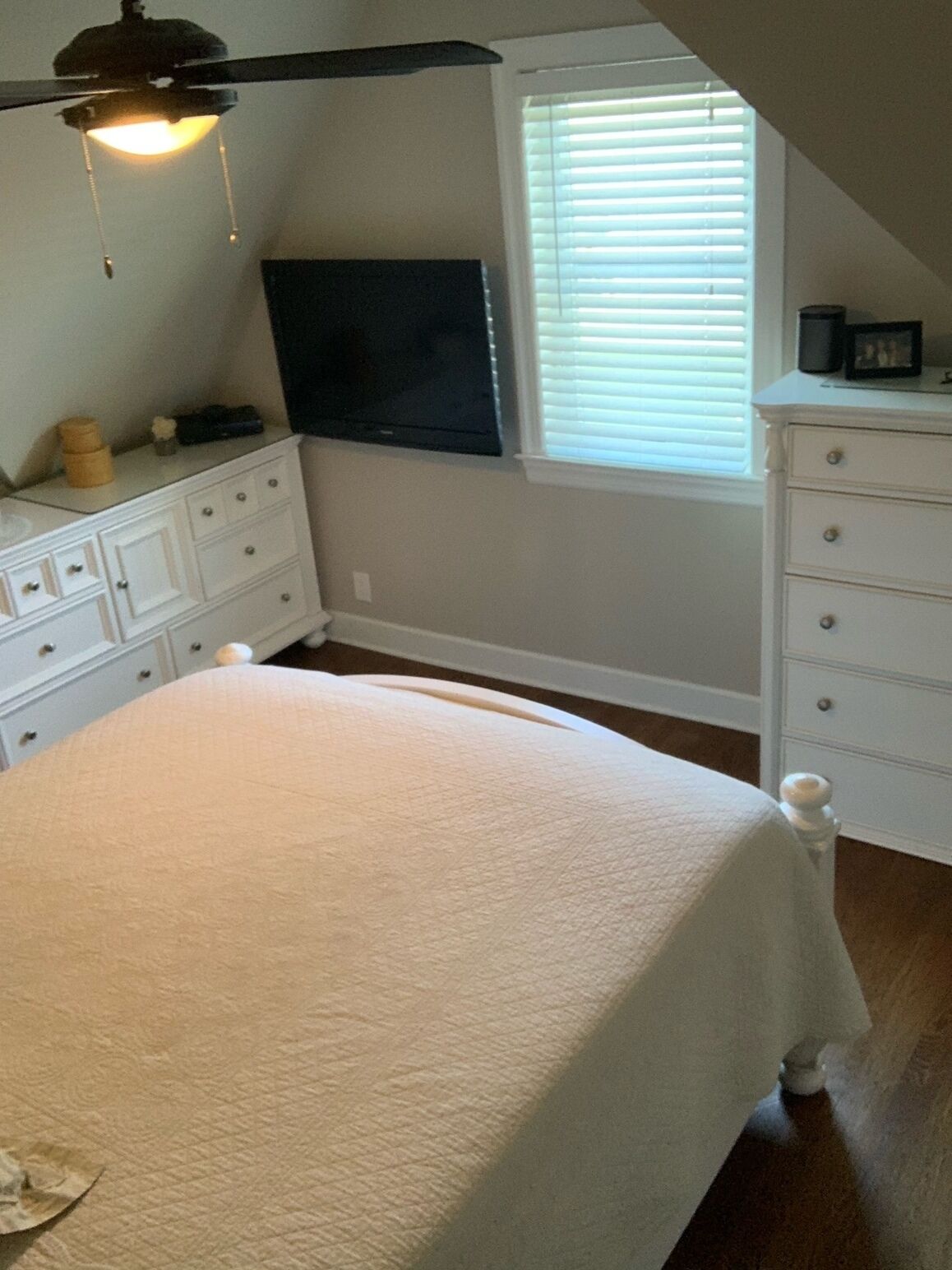 Ein Schlafzimmer mit Bett, Kommode, Fernseher und einem Fenster mit Jalousien.