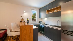 A modern kitchen with dark cabinets, a stainless steel refrigerator, a microwave, and a sink. There is a wooden island with chairs and a bottle of wine. - Amazing apartment in Stari Grad with WiFi (Stari Grad)