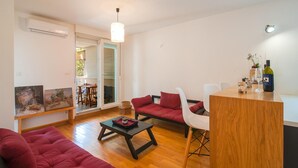 A modern living room with a wooden floor, red sofas, a small dining table, and a kitchen area with a wine bottle and glasses. - Amazing apartment in Stari Grad with WiFi (Stari Grad)