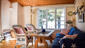 Ein gemütliches Zimmer mit Korbstühlen, einem blauen Sofa, einem Holztisch und einem großen Fenster mit Blick auf Bäume.