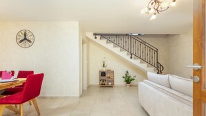 A dining area with a wooden table and red chairs, a staircase with a metal railing, and a white sofa in a living space. - Beautiful home in Rojnici (Rojnici)