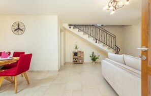 A dining area with a wooden table and red chairs, a staircase with a metal railing, and a white sofa in a living space.