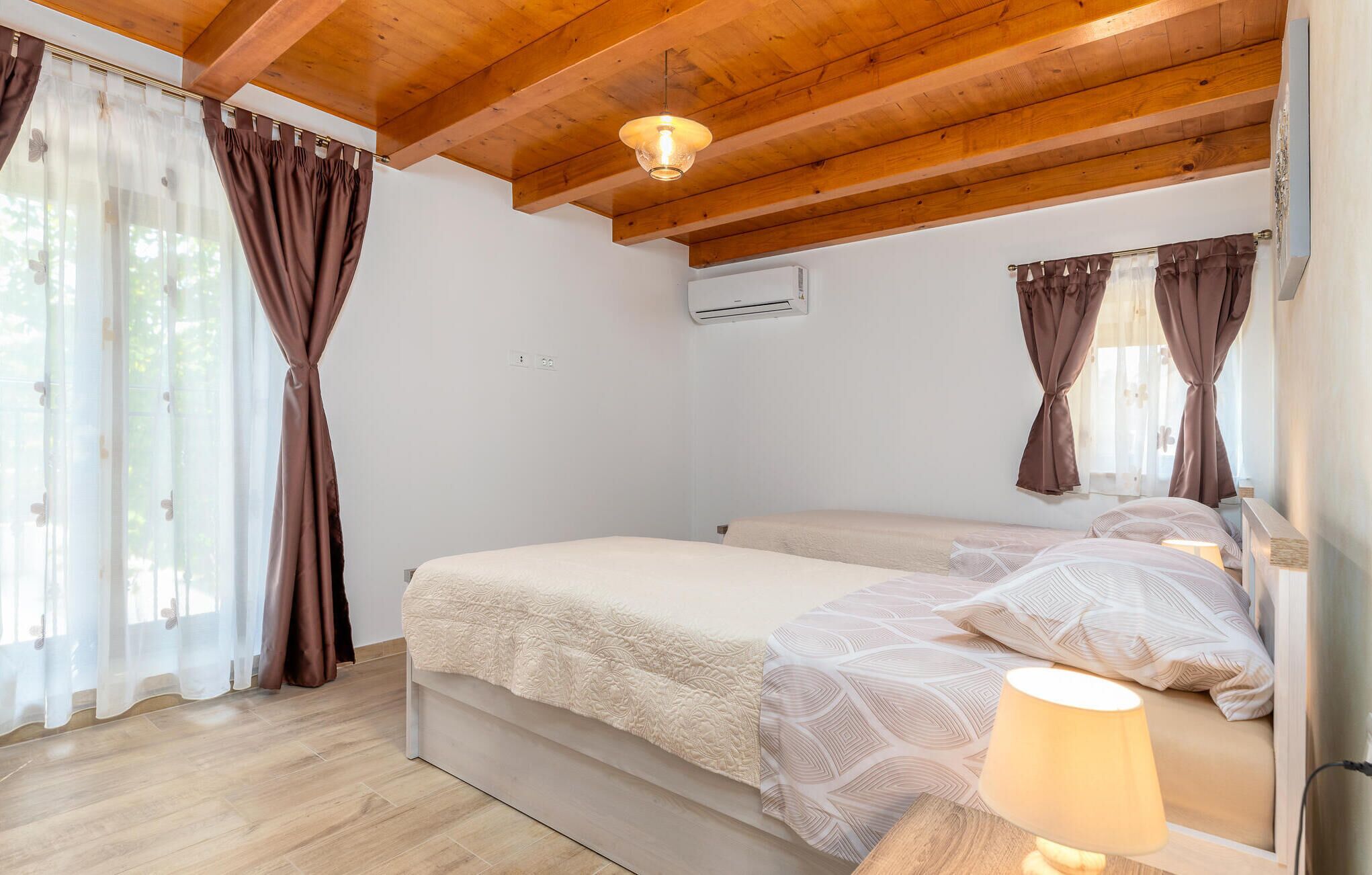 Une chambre avec un plafond en bois, un lit avec une literie à motifs, une lampe de chevet et des rideaux.