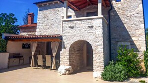 A stone building with a covered patio area, featuring a stone archway and a small table with chairs. - Beautiful home in Rojnici (Rojnici)