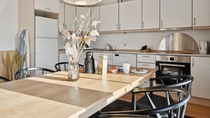 Een moderne keuken met witte kasten, een houten eettafel en een vaas met gedroogde bloemen.