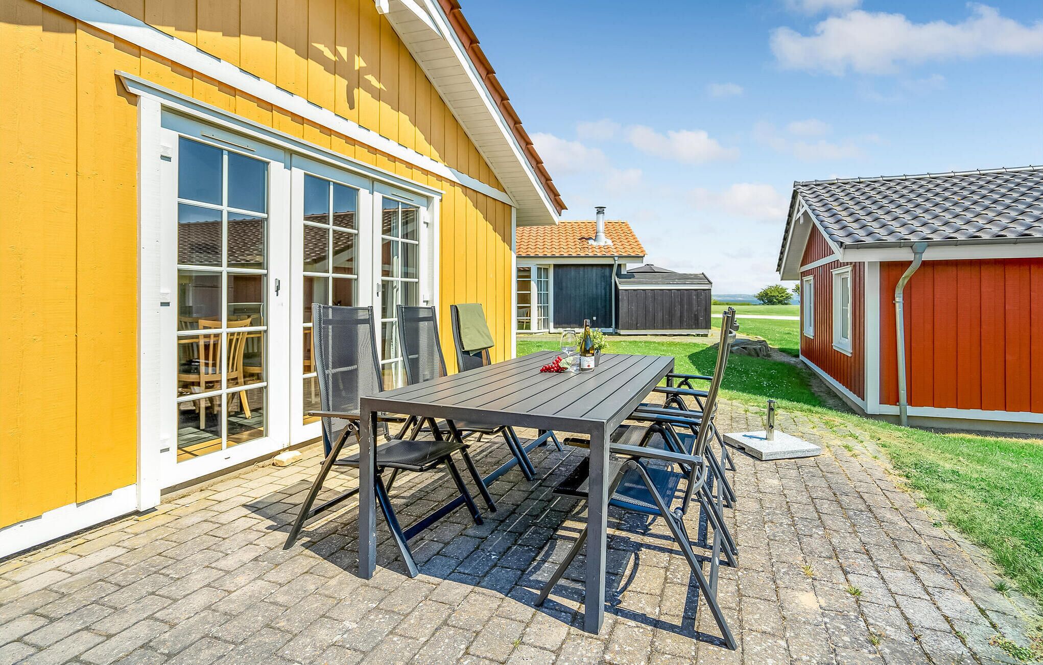 A patio with a table and chairs, a yellow building with large windows, and a red building in the background.