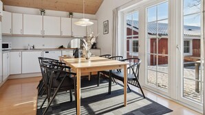 Een moderne keuken met witte kasten, een houten eettafel en zwarte stoelen. Er is een groot raam met uitzicht op een rood gebouw en een besneeerd landschap.