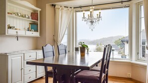 A dining area with a large table, chairs, a chandelier, and a view of a lake through a large window. - Cozy home in Aksdal with house sea view (Aksdal)