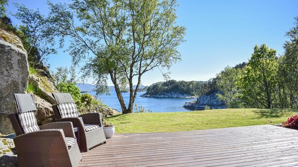 A wooden deck with wicker furniture and a view of a lake and rocky coastline. - Cozy home in Aksdal with house sea view (Aksdal)