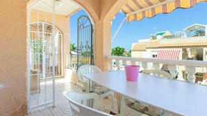 A balcony with a white table and chairs, a pink cup, and a view of buildings and greenery.