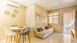 A living room with a beige sofa, a dining table with chairs, and a window with curtains.