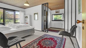 Ein modernes Schlafzimmer mit einem Bett, einem Sessel, einem roten Teppich mit Muster, einem weißen Kleiderschrank und einem Fenster mit Blick ins Grüne.