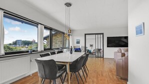 Ein moderner Essbereich mit großem Tisch, schwarzen Stühlen und Blick auf eine Stadtlandschaft durch hohe Fenster.