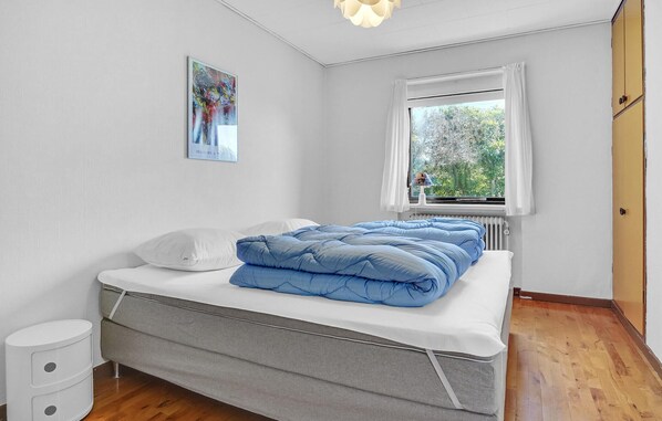 A bedroom with a bed, a window with a view of trees, a radiator, and a white wall with a framed picture.