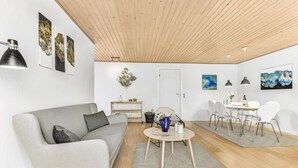 Un salon moderne avec un canapé gris, une table basse et un coin repas avec des chaises blanches.