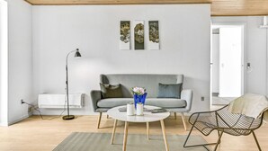 Un salon moderne avec un canapé gris, une table basse ronde et une chaise en métal. On y trouve une lampe sur pied et un vase avec des fleurs sur la table.