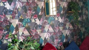 A room with a geometric floral wallpaper, a small arched mirror, a potted plant, and red and blue cushions. - Stockton Moors (Stockton-on-Tees)