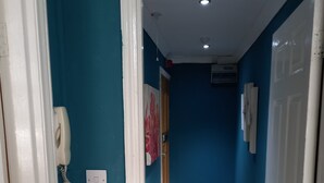 A hallway with teal walls, a wooden floor, and white trim. There is a door on the right and a phone on the left. - Stockton Moors (Stockton-on-Tees)