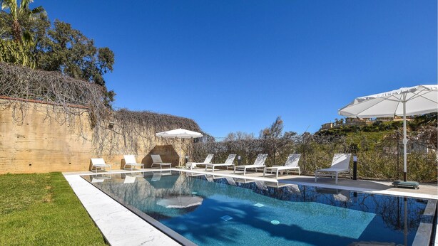 A clear swimming pool with lounge chairs and umbrellas, surrounded by a stone wall and greenery. - Lovely home in Balestrate (Balestrate)