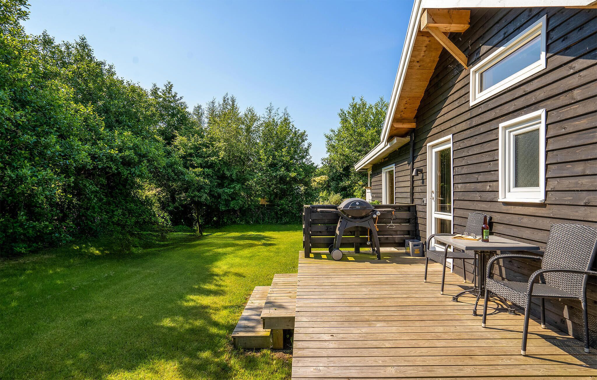 A wooden deck with outdoor furniture, a barbecue grill, and a glass door leading to a room.