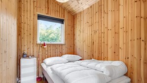 A wooden room with a bed, a window, and a bedside table with a lamp.