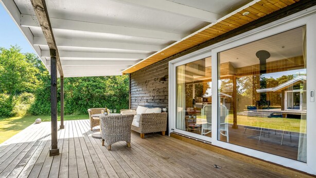 A covered patio with wicker furniture, a wooden deck, and a glass door leading to an interior space.