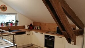 Una cocina con armarios blancos, encimera de madera, suelo a cuadros y techo con vigas de madera.