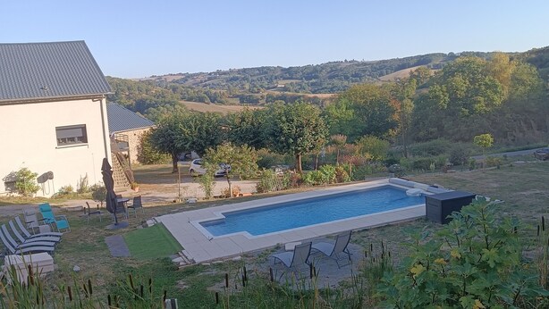 Una piscina con sillones de descanso, un edificio blanco y un paisaje montañoso al fondo.