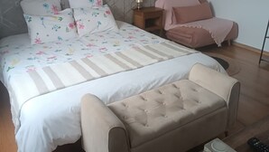 Un dormitorio con cama, mesita de noche, sillón y una pequeña mesa con control remoto.