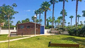 A small brick building with a blue door, surrounded by a well-maintained lawn and tall palm trees. - Gorgeous apartment in Oropesa del Mar with sauna (Oropesa del Mar)