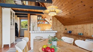 A wooden interior with a dining table set for two, a kitchen area with shelves, and a view through a door. - Amazing home in Sjællands Odde (Sjællands Odde)