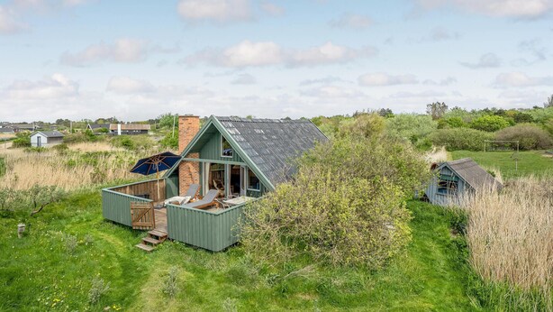 A small, green-roofed cabin with a deck and outdoor seating, surrounded by natural vegetation and a clear sky. - Amazing home in Sjællands Odde (Sjællands Odde)