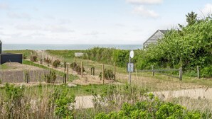 A coastal property with a sandy beach, a wooden structure, and a grassy area with a fence. - Amazing home in Sjællands Odde (Sjællands Odde)