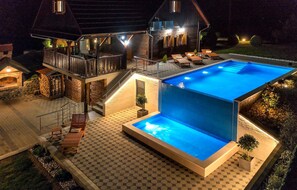 A modern outdoor pool area with a hexagonal tiled deck, a wooden deck with lounge chairs, and a stone fireplace. - Lovely home in Bedenica (Bedenica)