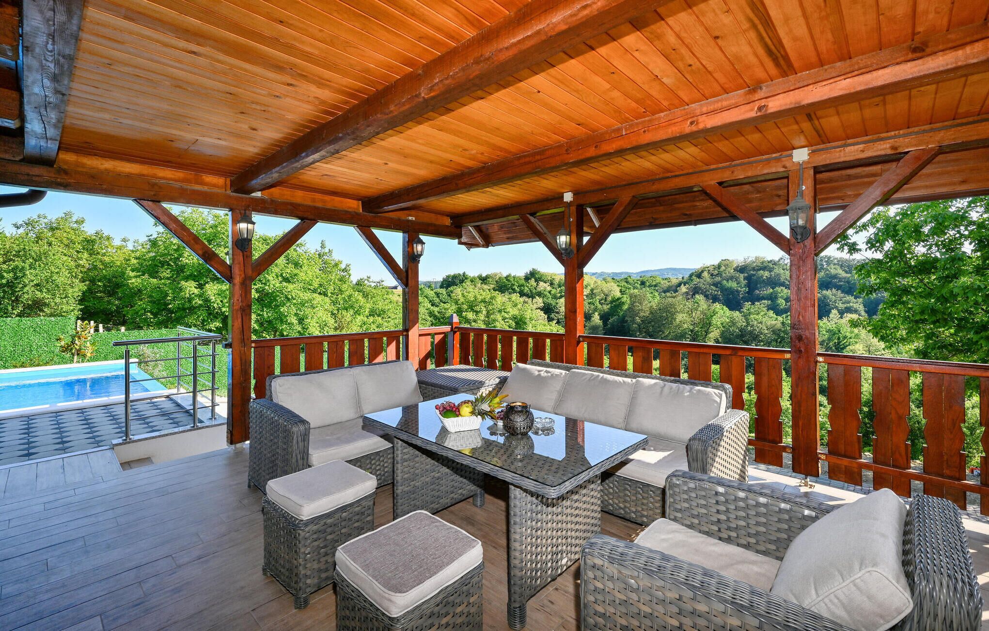 Une terrasse extérieure avec des meubles en osier, une table en verre et une piscine.
